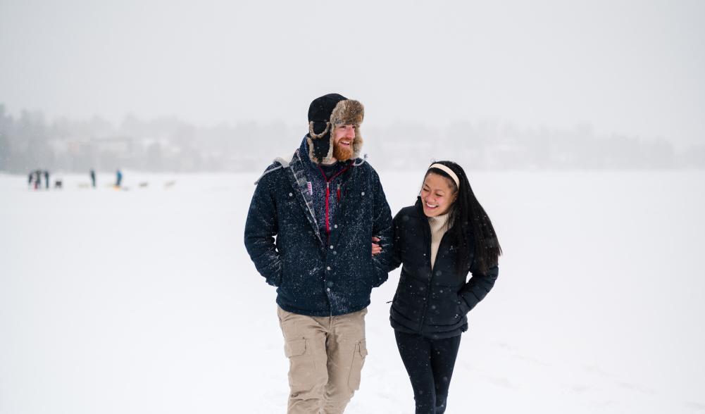 Man and woman walk arm and arm on frozen lake in snowstorm