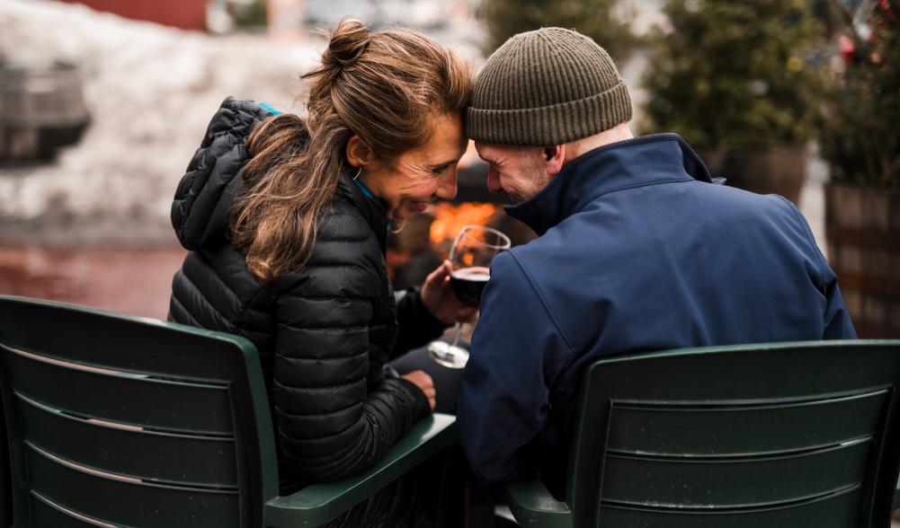 Couple sit head to head in Adirondack chairs by fire