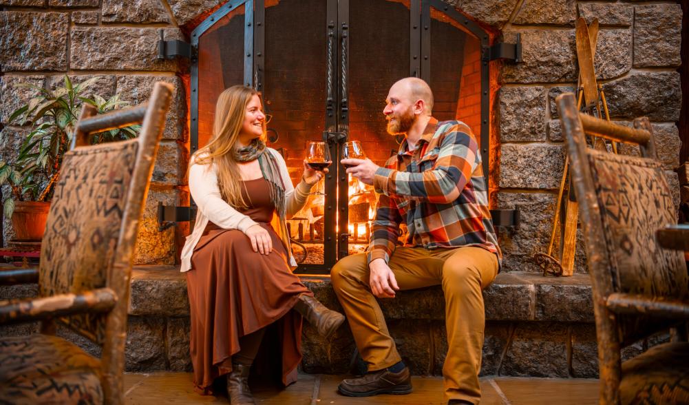 Man and woman cheers glasses sitting in front of stone fireplace