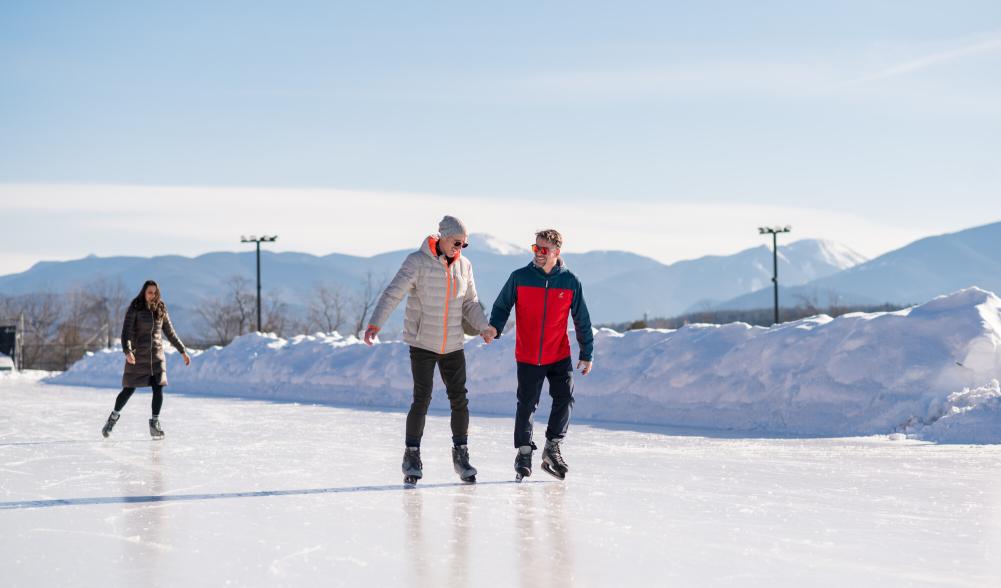 Two men ice skate on outdoor track holding hands