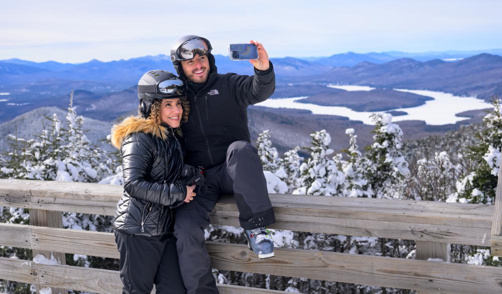 Man takes selfie of himself and woman in ski gear on mountain observation deck