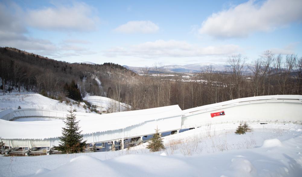 Red bobsled slides down track with mountains in background