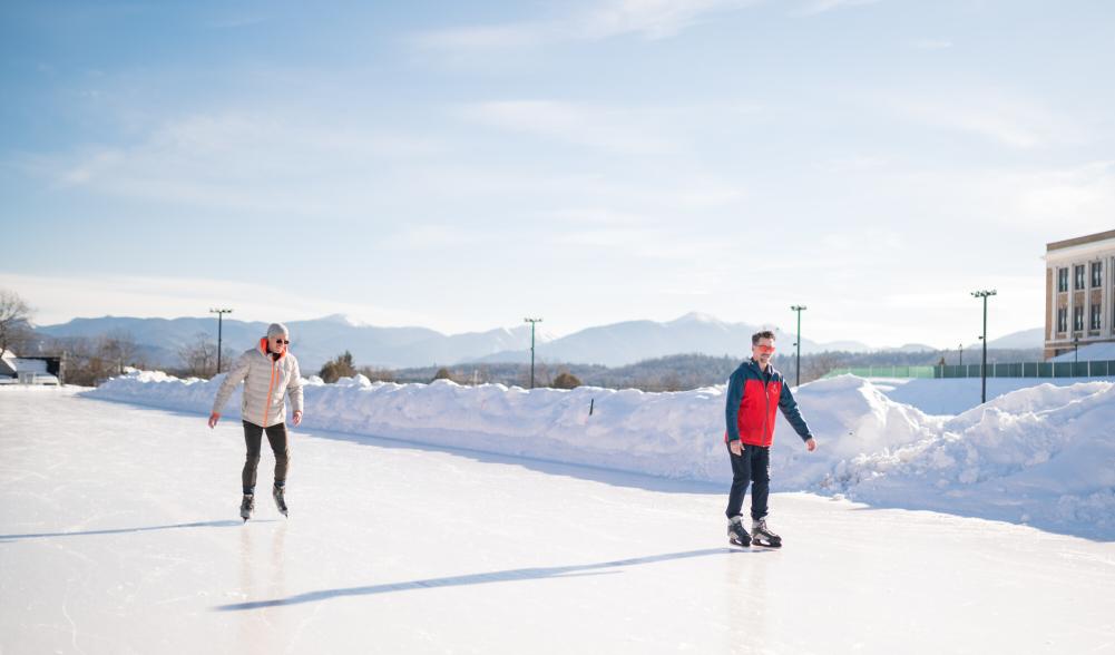 Two men ice skate on Olympic Oval on snowy bluebird day