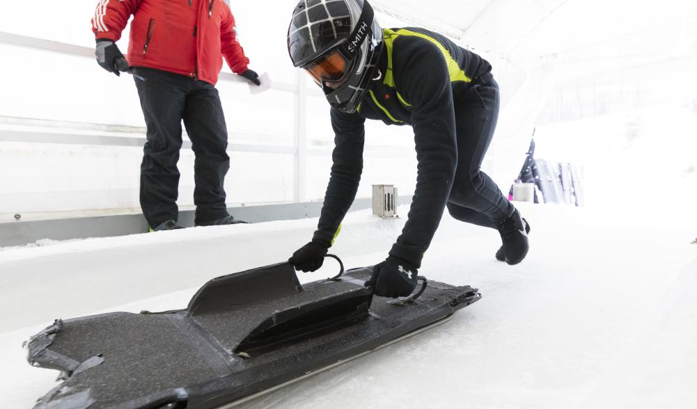 Person in helmet runs down track with skeleton sled in hand