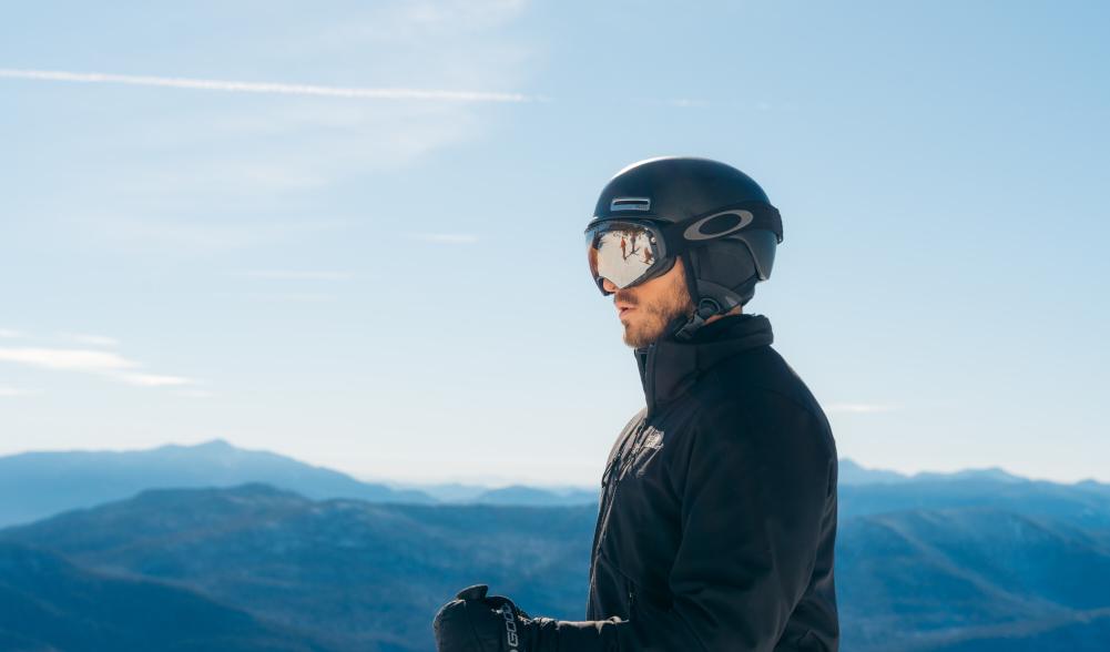 Man looks at view from top of mountain wearing ski helmet and goggles