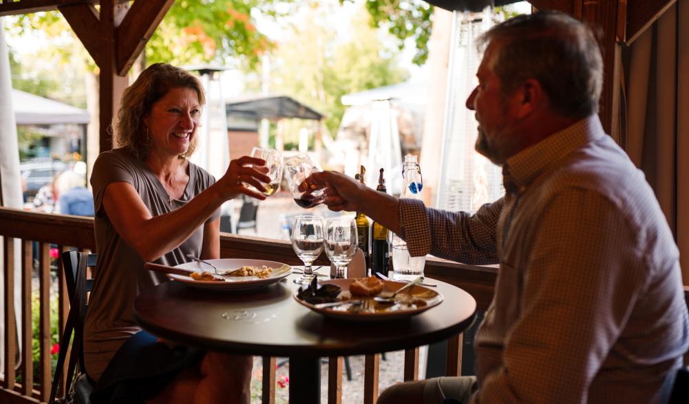 A couple sitting on a patio, smiling and raising their glasses at Amado restaurant.