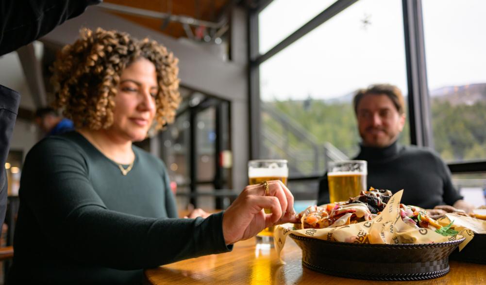 A woman with very curly hair takes a bite from nachos.