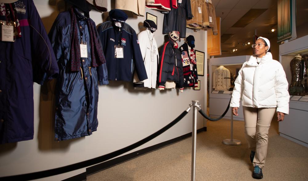 A woman in a white winter coat looks at vintage Olympic clothing.