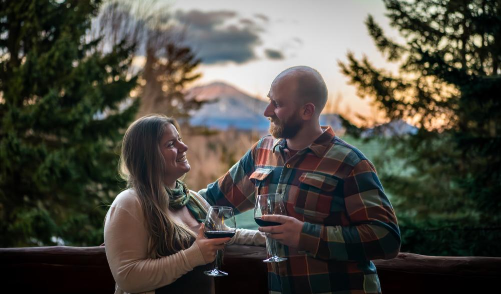 A man and woman toast drinks on a snowy balcony.