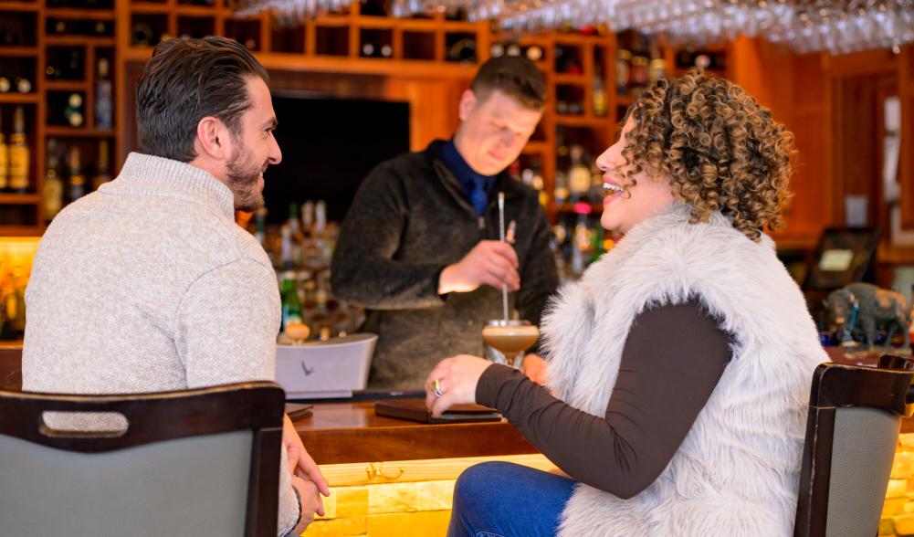 A man and woman enjoy drinks and food at a bar.