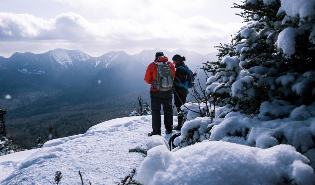 Two people in outdoor gear stand on the side of a mountain.