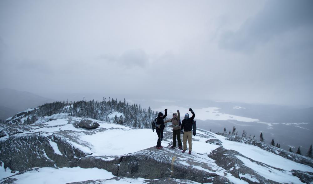 A group of hikers pose for a photo on top of Ampersand Mountain in the winter