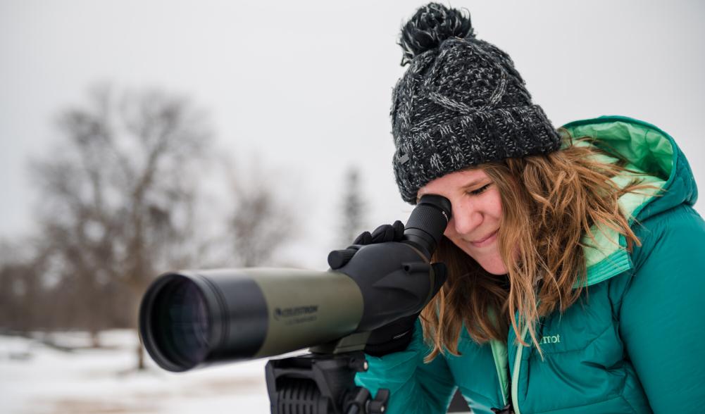 A birder looking through a spotting scope in the winter