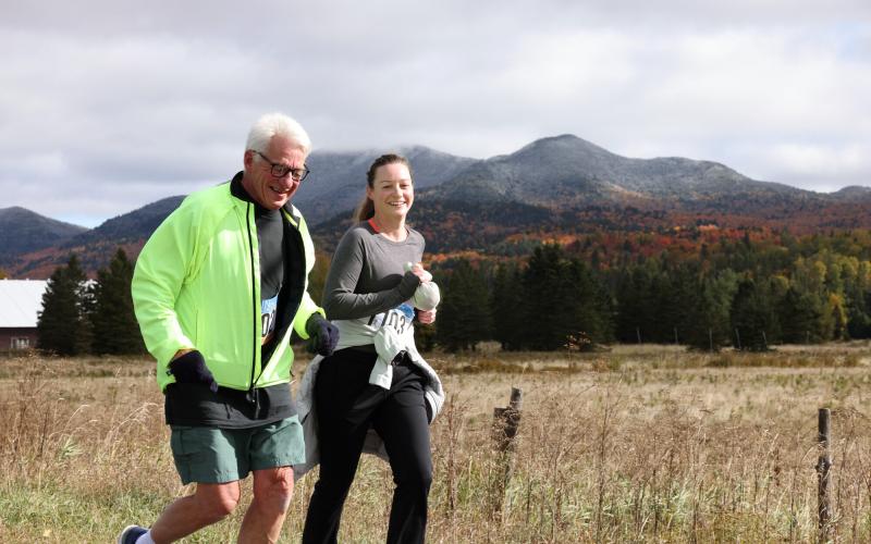 Man and woman running side by side on road with mountain in background