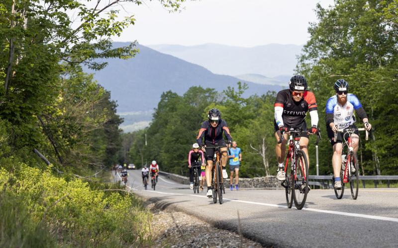 A group of cyclists going up a road with mountains behind them