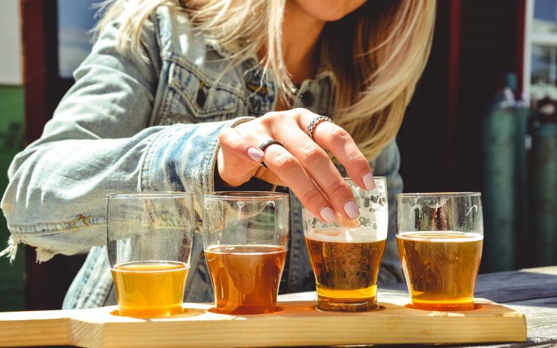 A close-up of a woman reaching for a glass on a flight of beer.