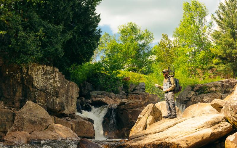A flyfisher on some rocks by the water