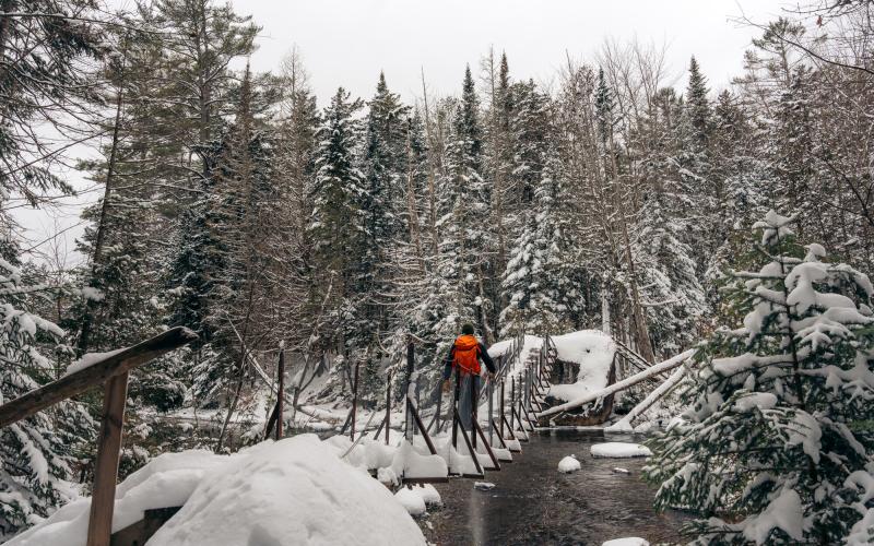 A snowshoer walks across a metal bridge