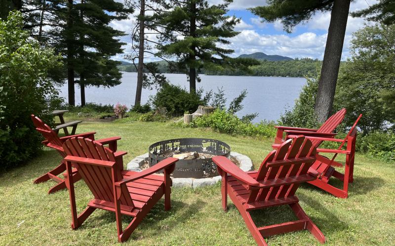 red adirondack chairs circle the firepit overlooking the lake through the trees