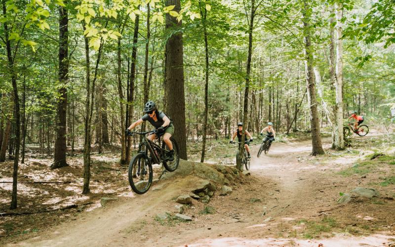 A bunch of people mountain biking over a ramp