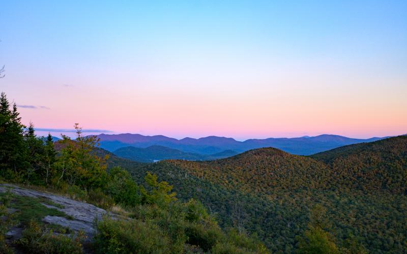 View from the summit of Haystack Mountain Mountain as the sun sets behind the silhouette of the Adirondack Mountains