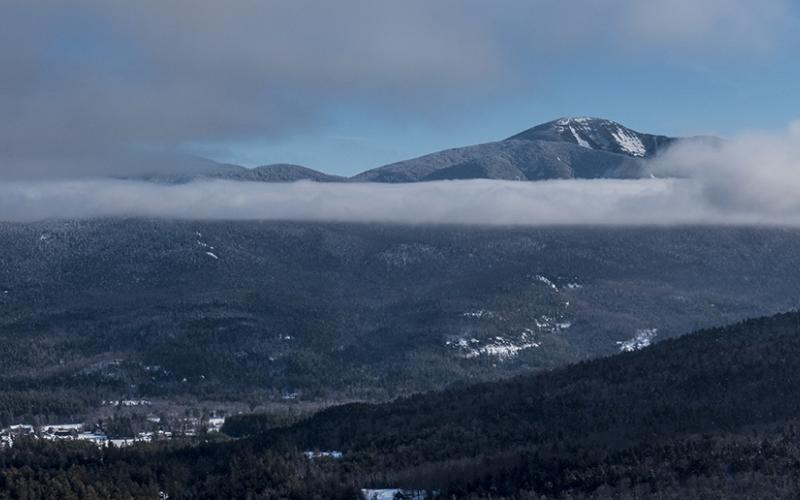 A tall mountain pokes through the clouds in the winter