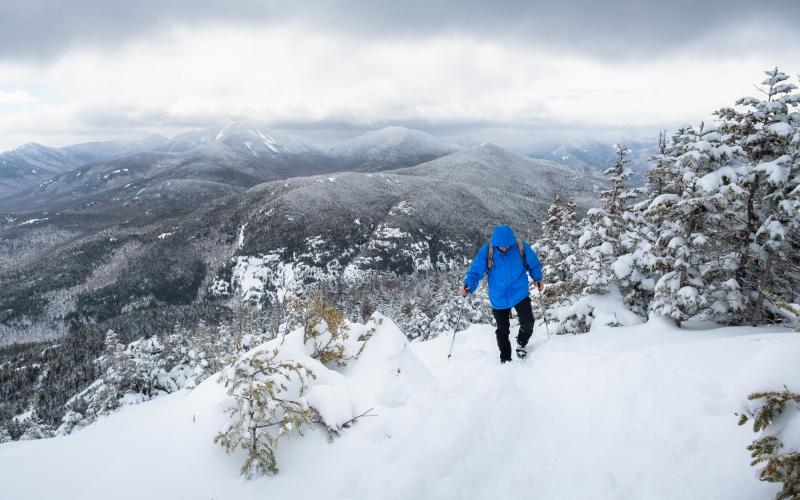 A man in a blue coat walks up a snowy mountain trail