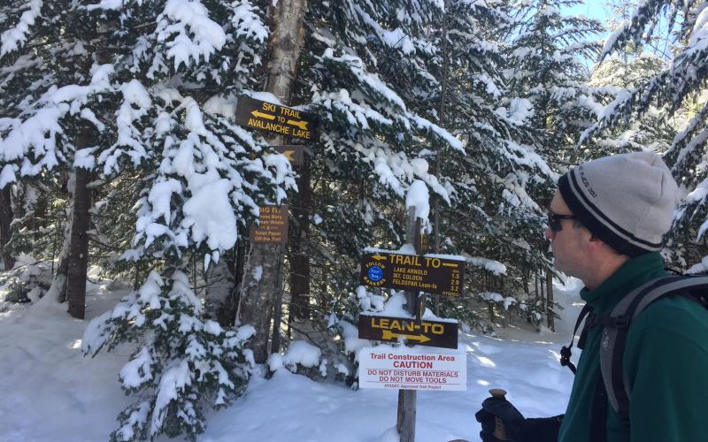 A hiker looking at wooden trail signs in the winter