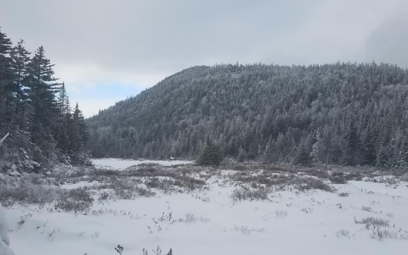 View of a snowy ridge from a frozen over pond