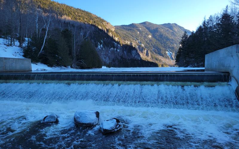 A long dam with water spilling over the top in the winter