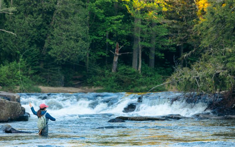 A fly fisher casts out at the bottom of a short waterfall