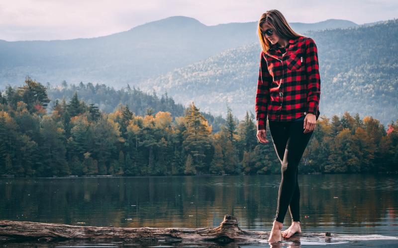 A woman walks on a log in a pond