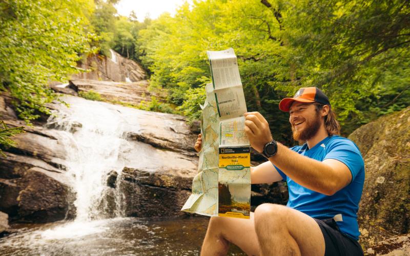 A hiker checks his map in front of a waterfall