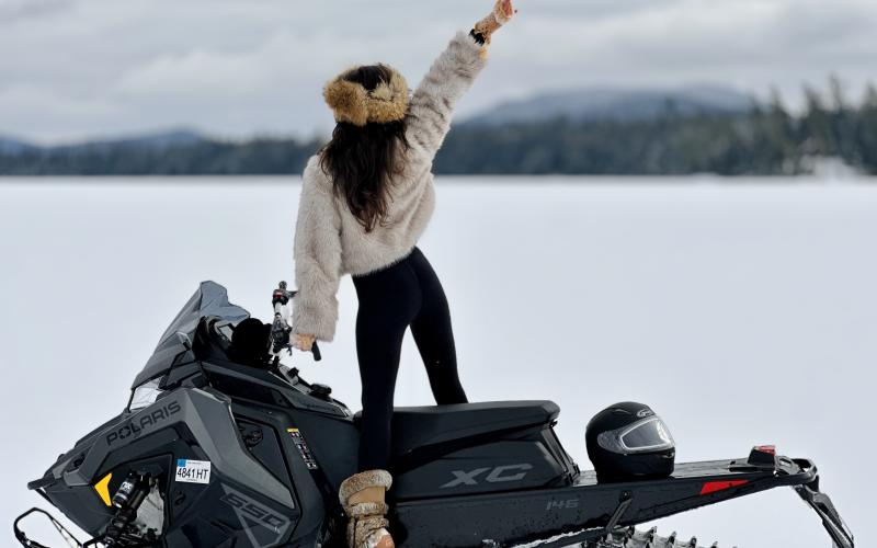 excited girl in furs looks out over the snowy landscape from atop a polaris snowmachinewith mountain backdrop