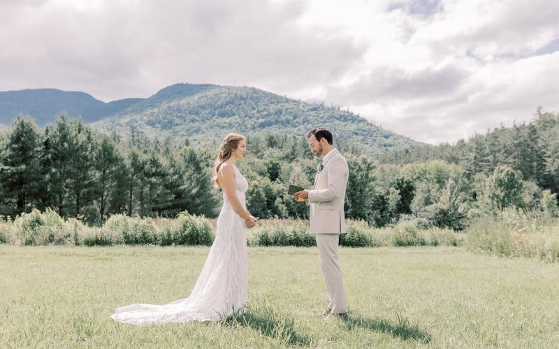 Bride and groom face each other in a grassy field with mountain views