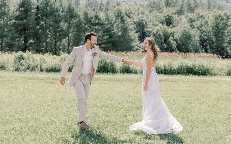 Bride and groom laugh and dance in a grassy field