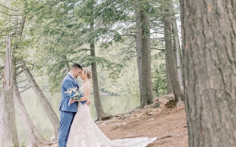 Bride and groom embrace surrounded by cedars next to a tranquil pond