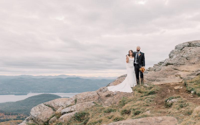 Bride and groom side hug on a rocky face overlooking the water