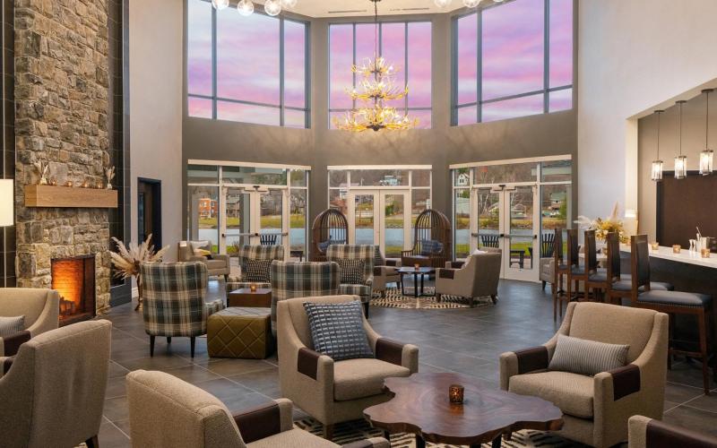 Grand lobby space with stone fireplace, plush armchairs and a view of the lake and mountains