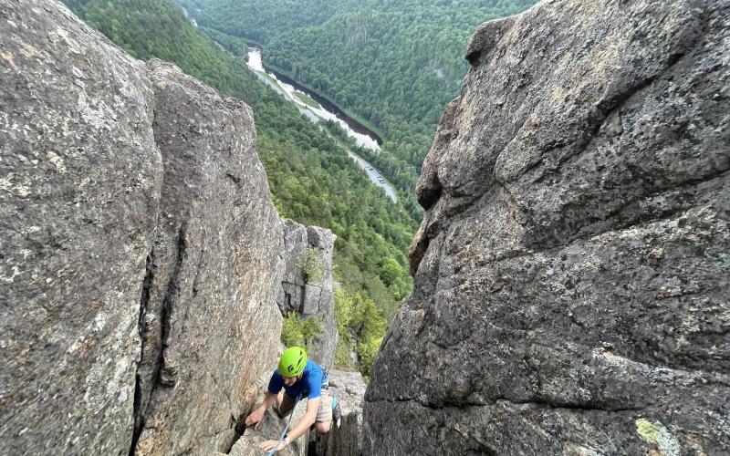 a rock climber ascends a crevice in the mountainside