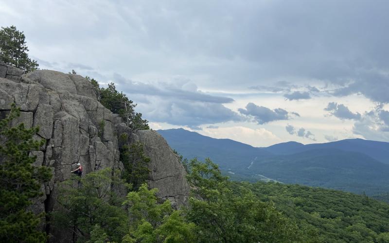 Mountain background while person climbs a shear cliff face in the forground