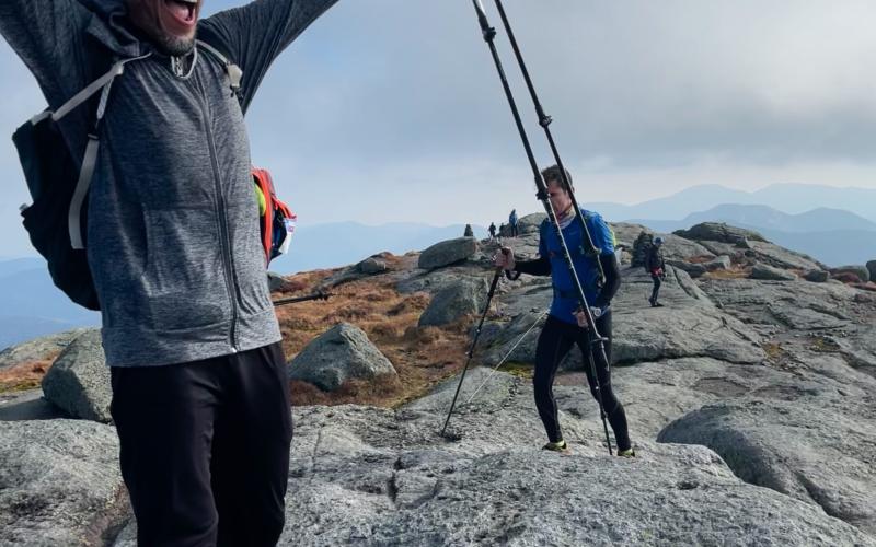 A very happy man raises his arm in sucess at the top of the summit