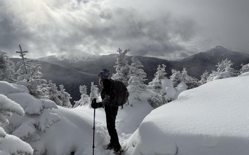 Snowshoer takes in the mountains in the distance, surrounded by pillows of beautiful snow and encrusted trees at the top of a peak