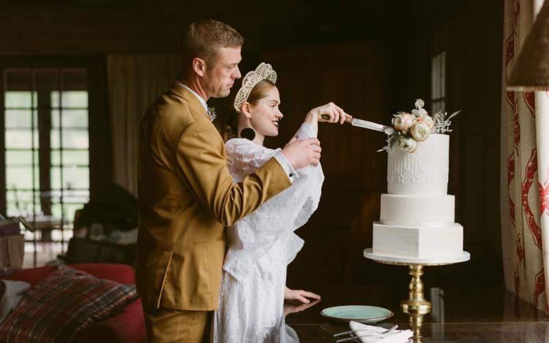 a bride and groom smile as they cut their wedding cake