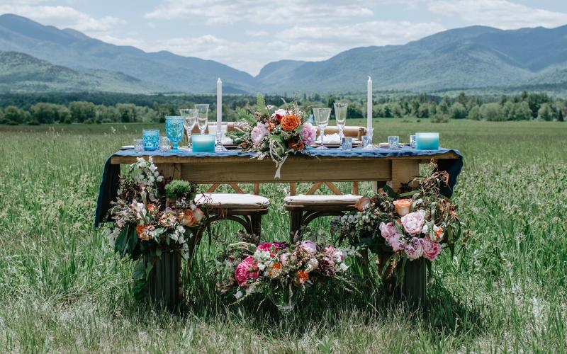 The Sweetheart table adorned with flowers, candles and blue glass in a meadow with the high peaks mountains in the background