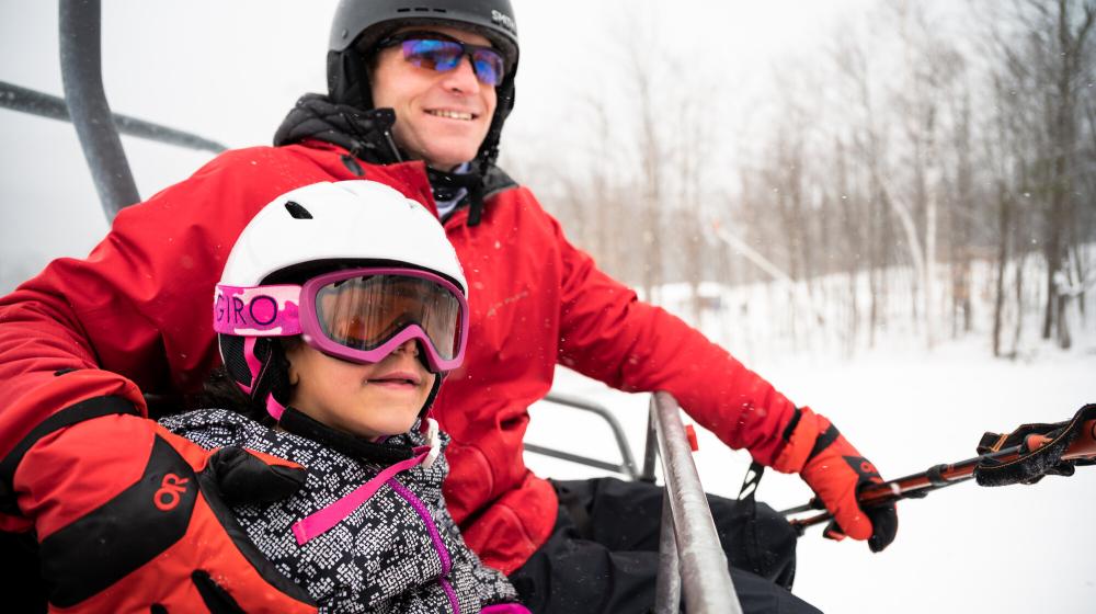 A father and daughter duo on a ski chair lift